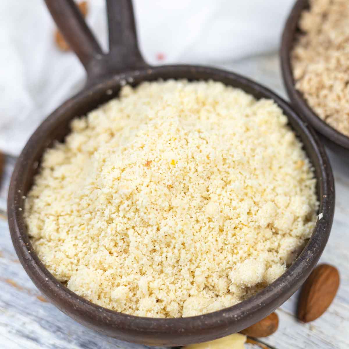 A close-up of a bowl of almond flour displayed on a wooden table.