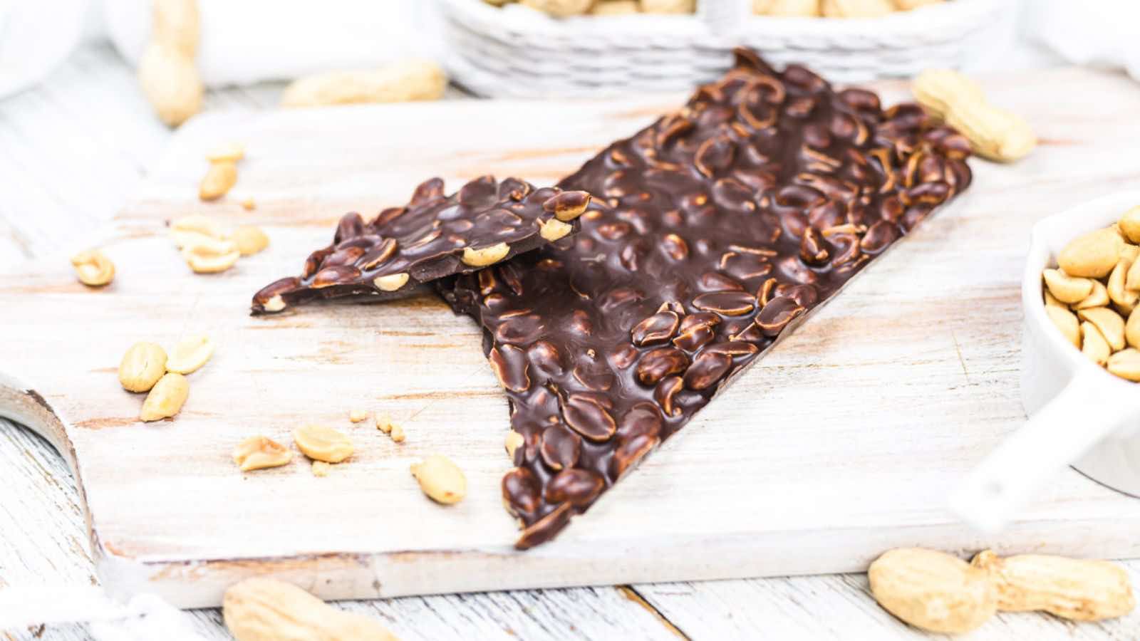 A piece of dark chocolate bark with peanuts on a wooden board.