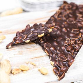 A piece of dark chocolate bark with nuts, resting on a wooden surface.