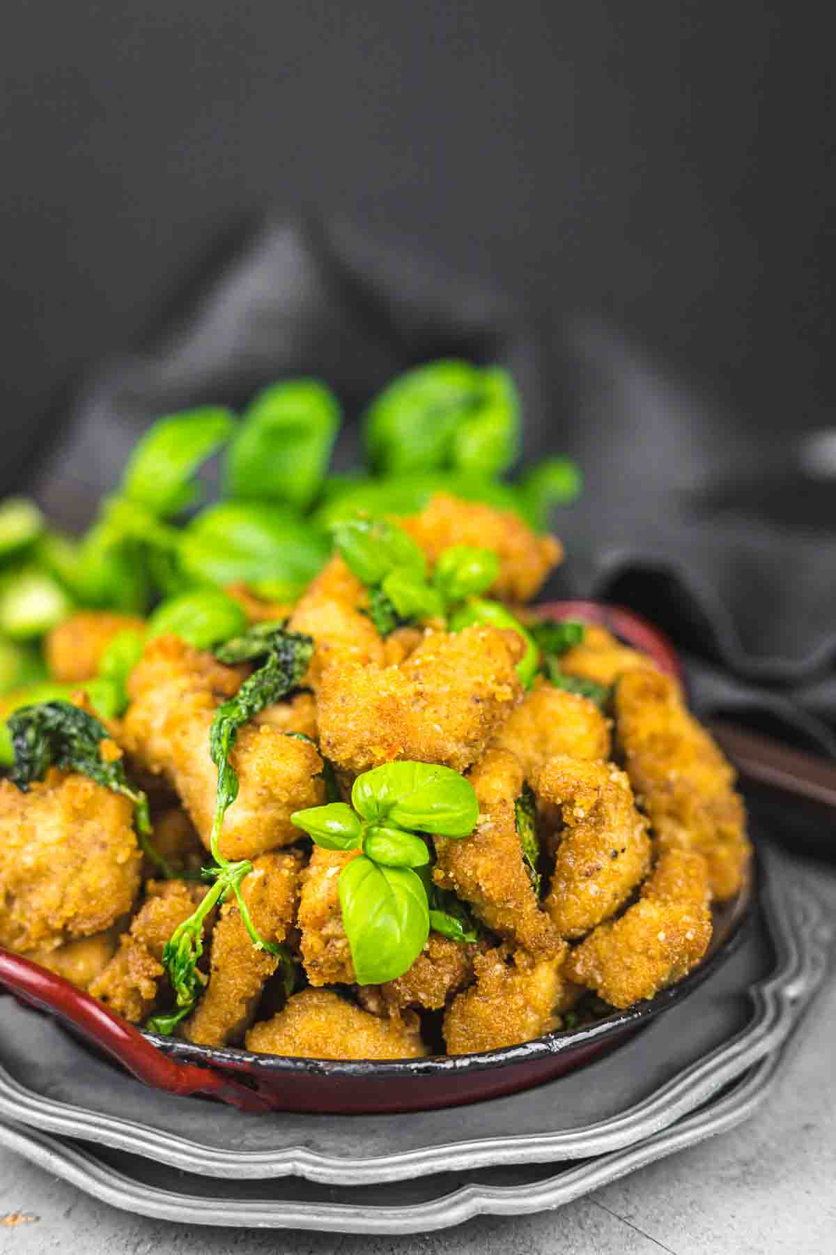 Breaded chicken pieces garnished with fresh basil in a black bowl on a gray surface.