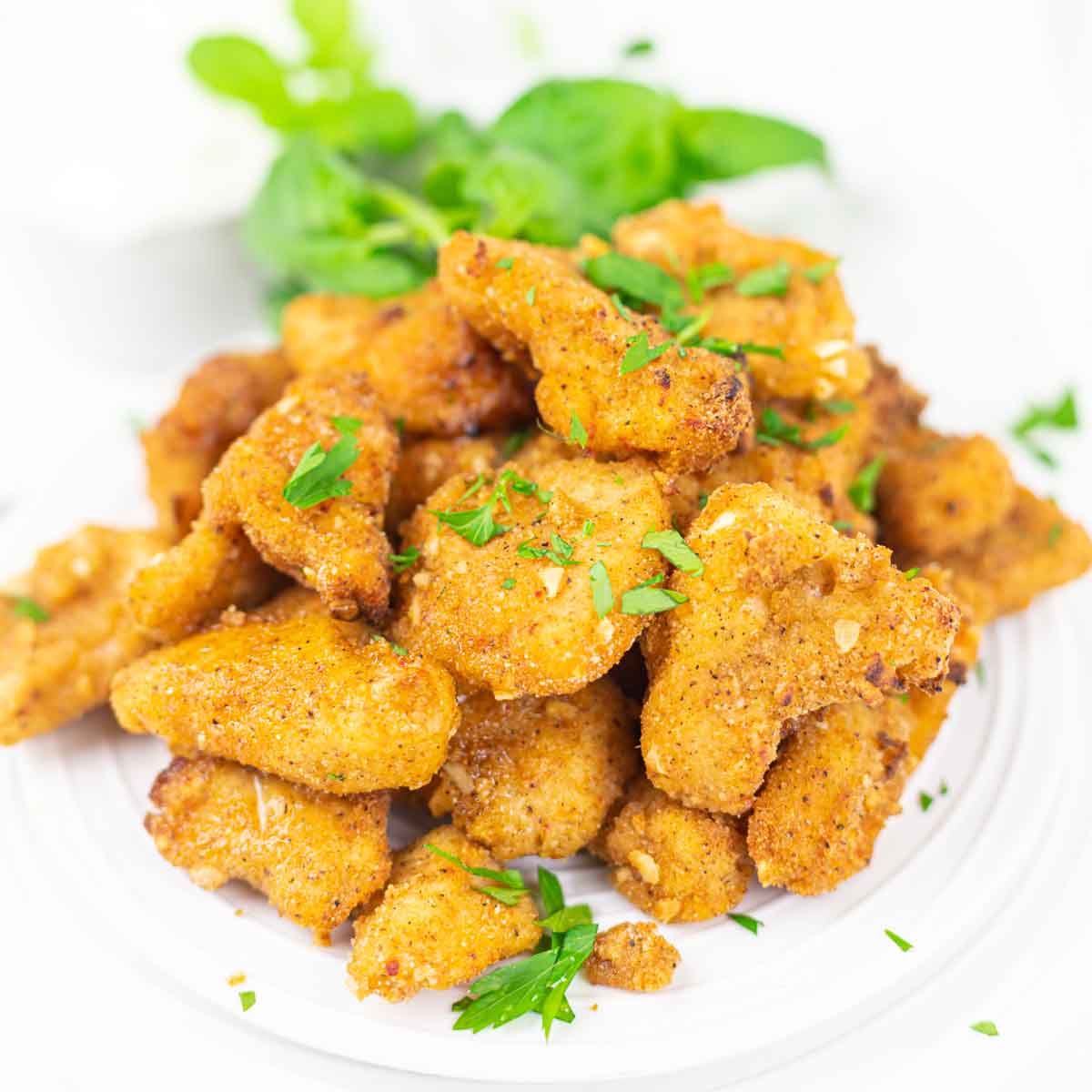 A plate of breaded and fried chicken pieces garnished with chopped herbs, displayed on a white background.