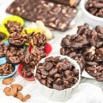 An assortment of chocolate-covered almonds and nuts displayed in bowls and colorful silicone cups on a light wooden surface.