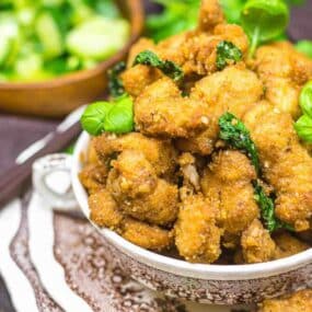 A bowl of crispy fried chicken garnished with basil leaves.