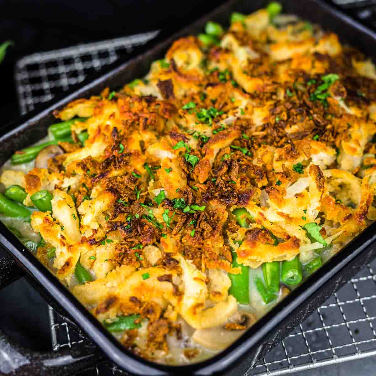 A casserole dish filled with a baked green bean casserole topped with crispy onions and chopped herbs.