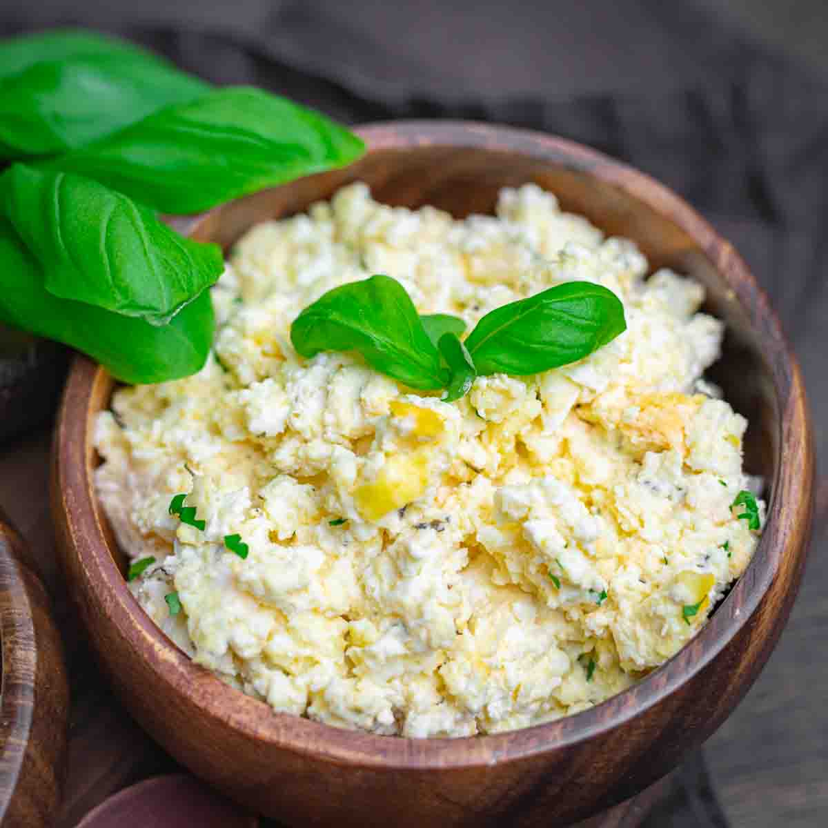 A wooden bowl filled with creamy cheese and herbs, topped with fresh basil leaves.