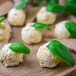 Cheese balls garnished with fresh basil leaves on a wooden platter.