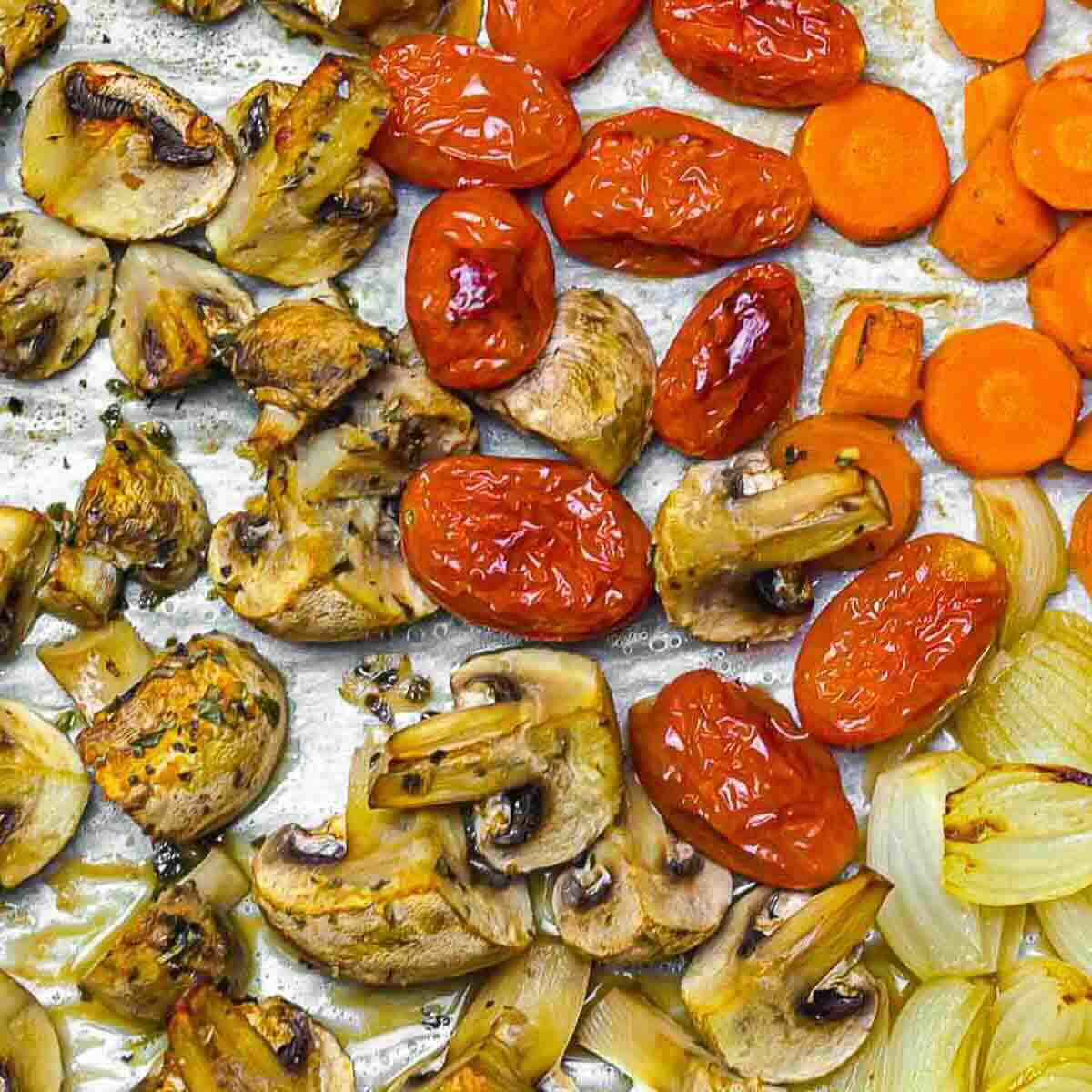 Roasted vegetables on a baking tray, including mushrooms, cherry tomatoes, carrots, and onions.