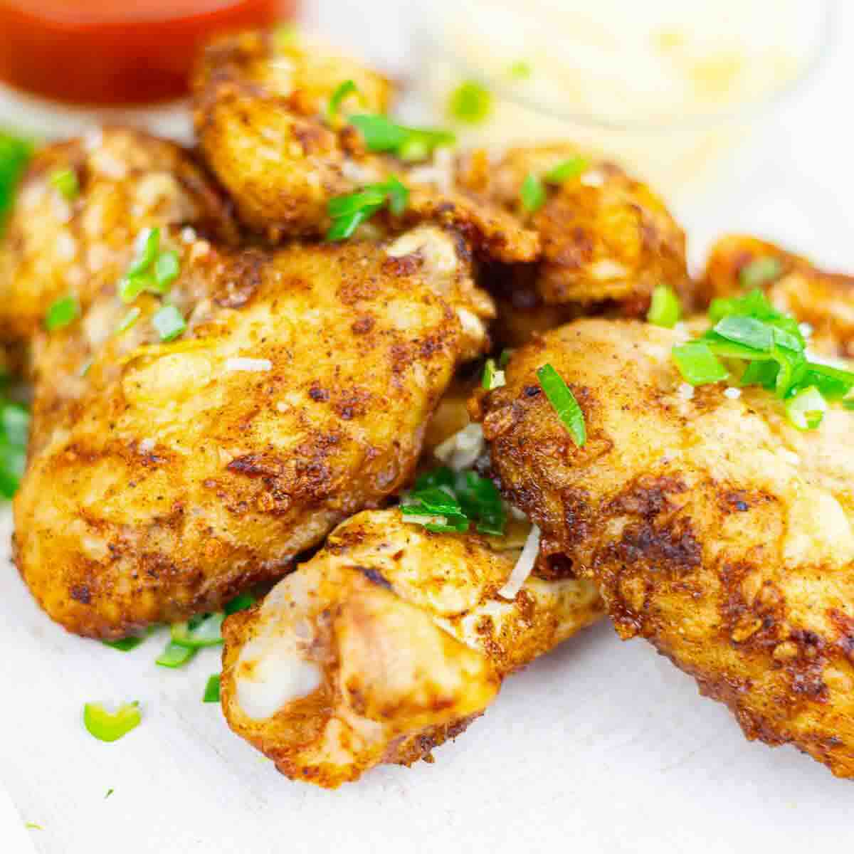 Close-up of six seasoned and baked chicken wings garnished with chopped green onions on a white surface.