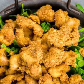 A bowl of golden-brown fried chicken pieces served on a bed of fresh green lettuce.