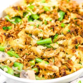A casserole dish contains a green bean casserole topped with crispy onions and mushrooms, garnished with herbs.
