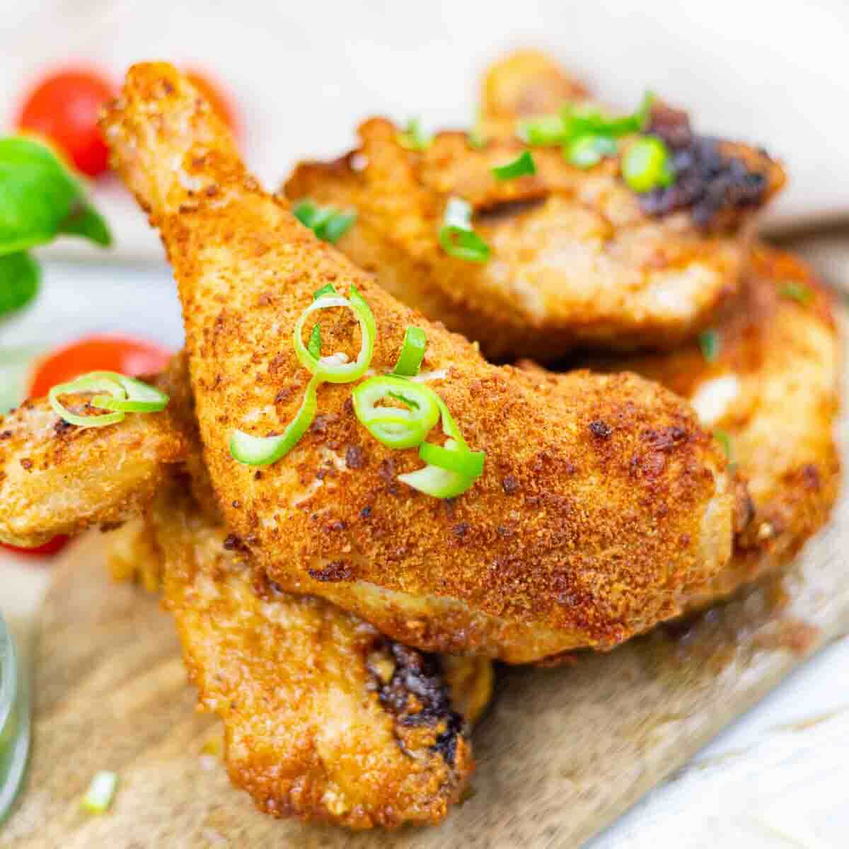 Close-up of crispy, seasoned chicken wings garnished with sliced green onions, served on a wooden board.