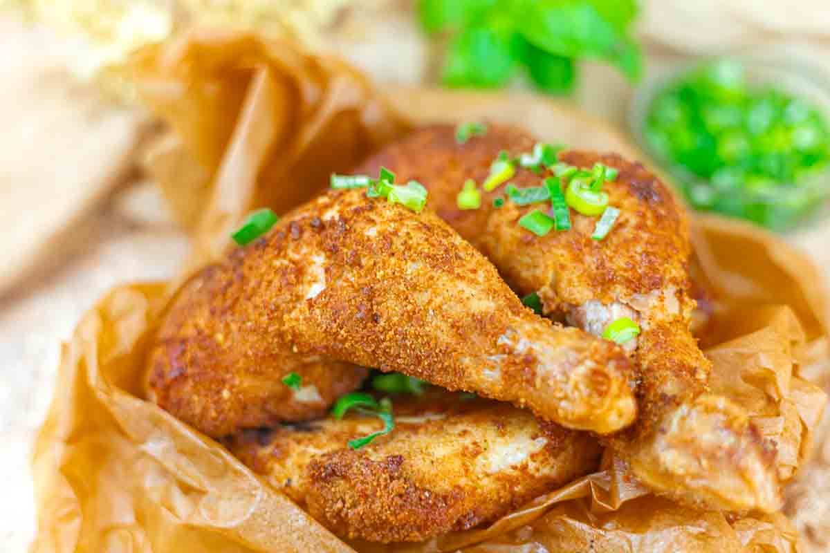 Two pieces of seasoned, baked chicken with crispy skin are garnished with chopped green onions and served on brown parchment paper.