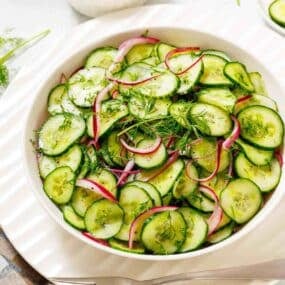 A bowl of cucumber salad with sliced cucumbers, red onions, and fresh dill, dressed lightly and served on a white plate.
