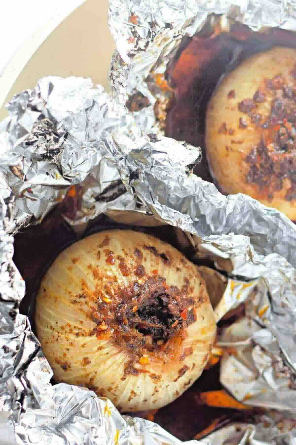 Two whole onions roasted with spices, wrapped in crinkled aluminum foil and partially unwrapped to show the cooked tops.