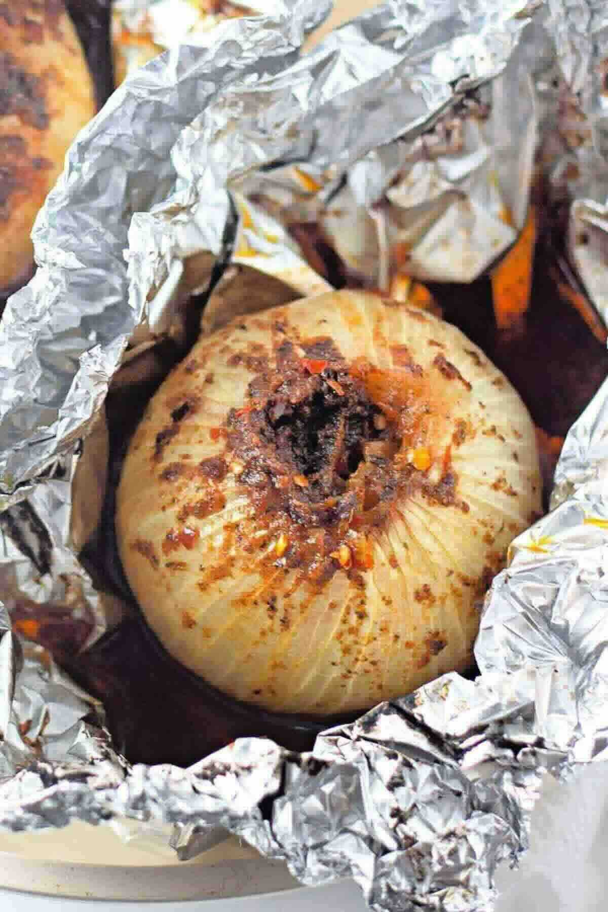 A whole baked onion with visible seasoning sits in a partially opened sheet of aluminum foil.