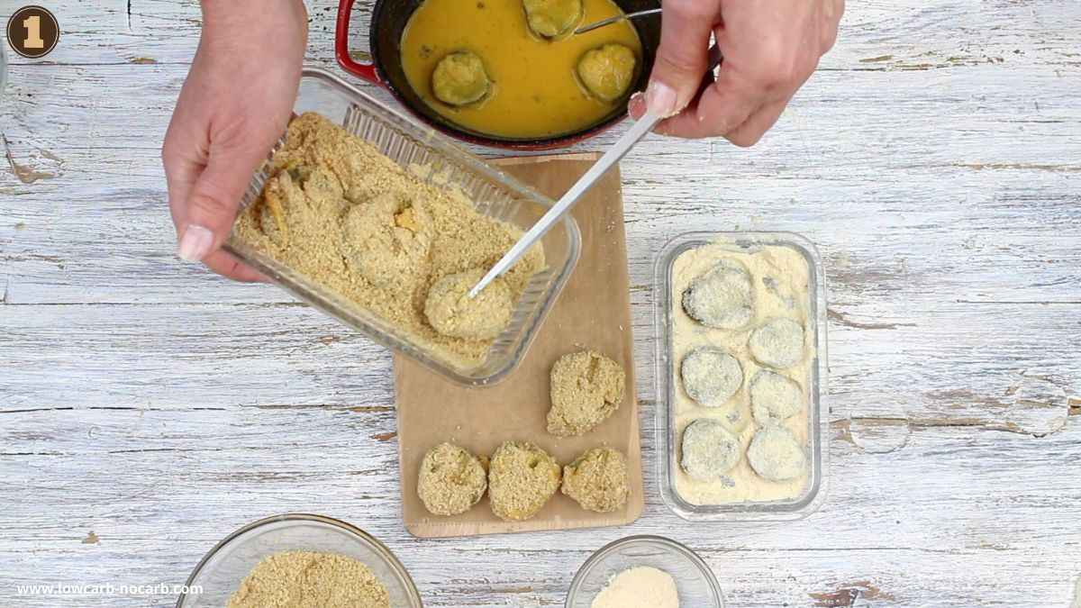 A person coats round food pieces in breadcrumbs, with bowls of egg wash, flour, and more breadcrumbs on a wooden surface.