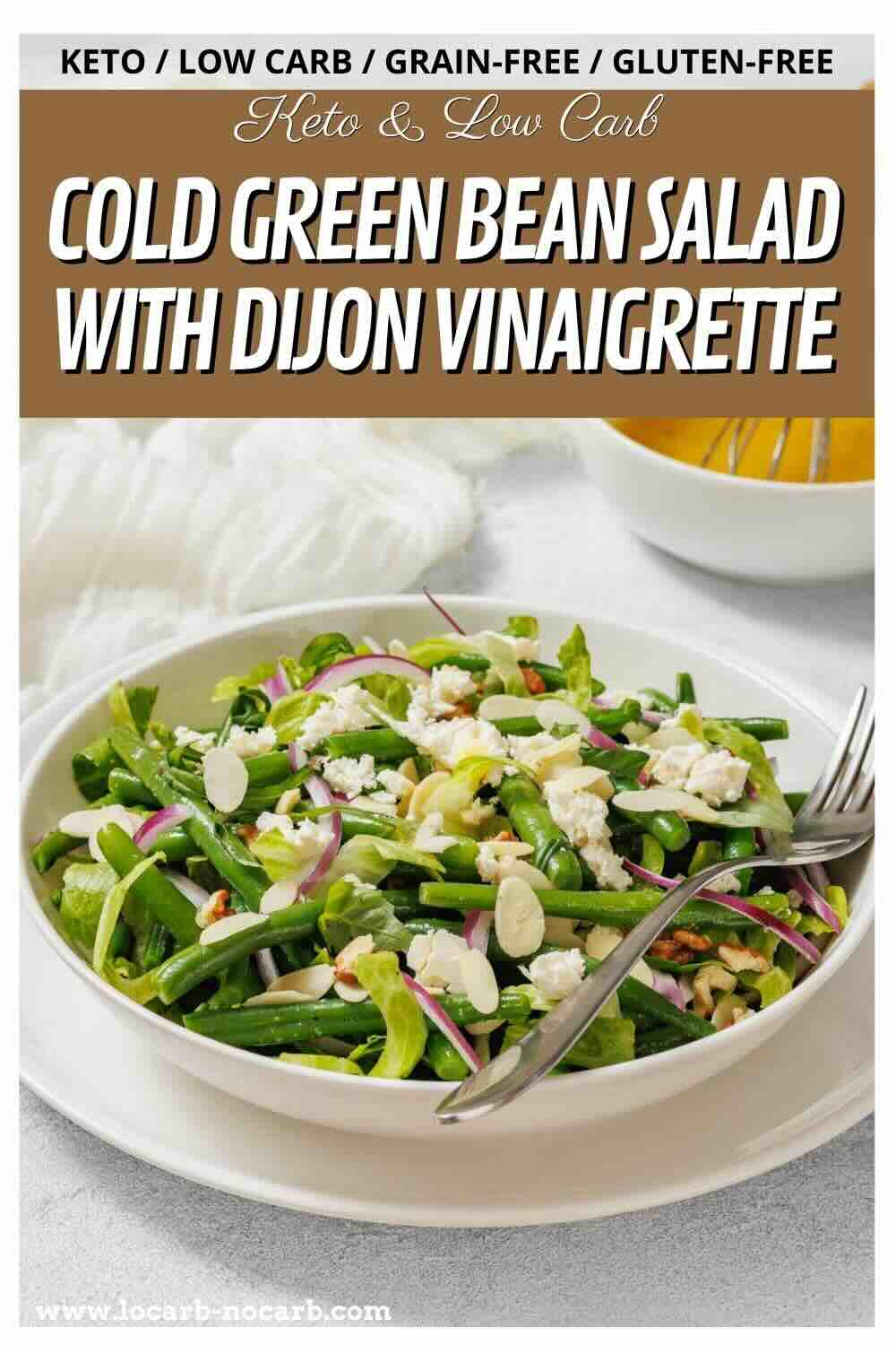 A plate of cold green bean salad with red onions, feta cheese, and nuts, served with a fork and dijon vinaigrette on the side.