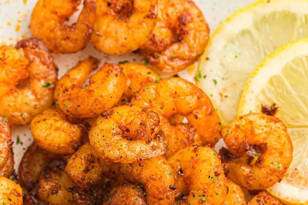 Seasoned cooked shrimp served with lemon slices on a white plate.