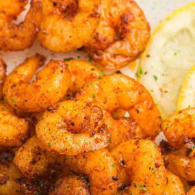Seasoned cooked shrimp served with lemon slices on a white plate.