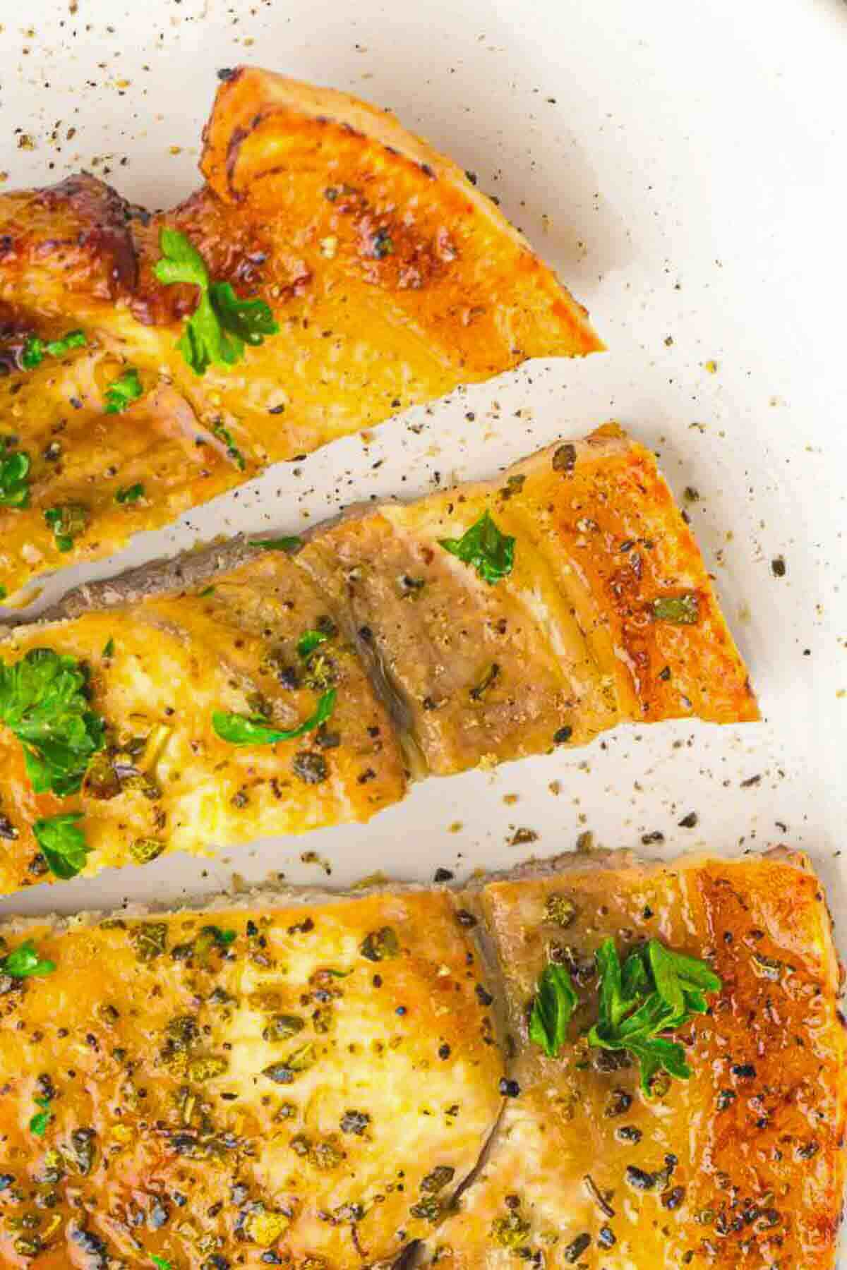 Close-up of three slices of cheesy, herb-topped pizza on a white surface, garnished with chopped parsley.