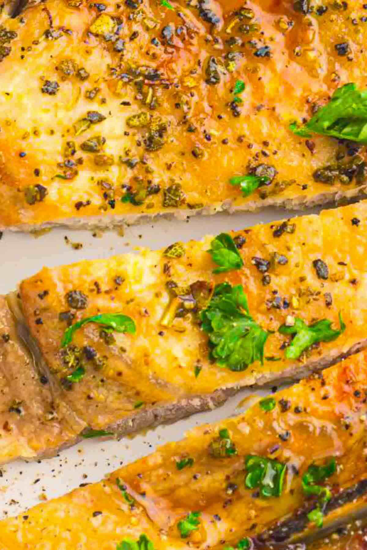 Close-up of cooked salmon fillets garnished with chopped herbs and cracked black pepper.