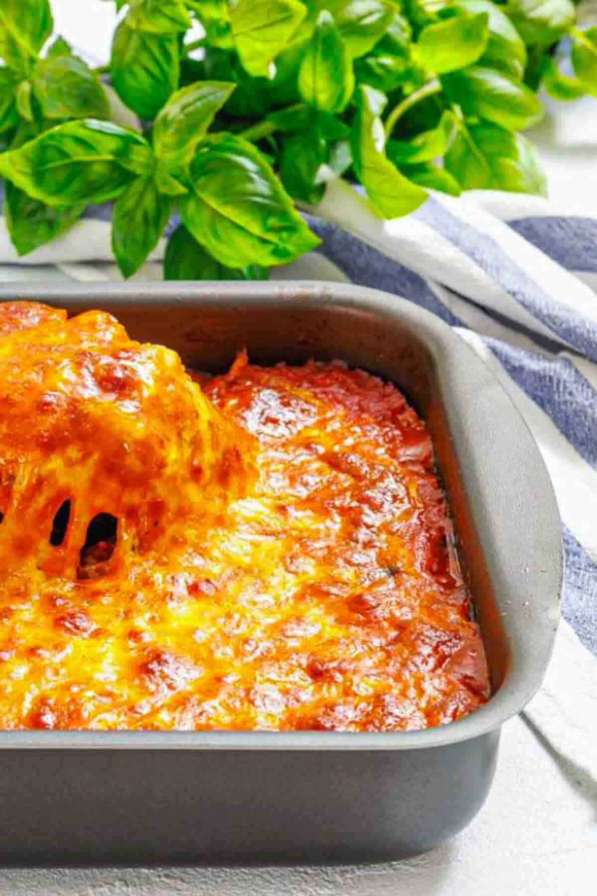Eggplant parmesan casserole with fresh basil background.