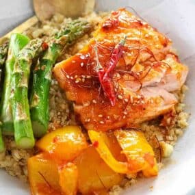 Grilled salmon with sesame seeds and chili, served with asparagus, yellow bell peppers, and a grain base.