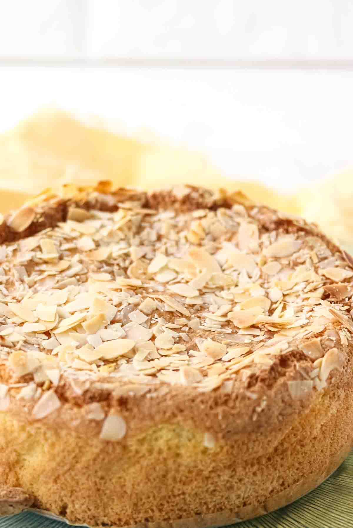 A close-up of a round almond cake topped with sliced almonds on a light-colored surface.