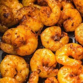 Close-up of cooked shrimp coated in a reddish-brown seasoning, arranged closely together.