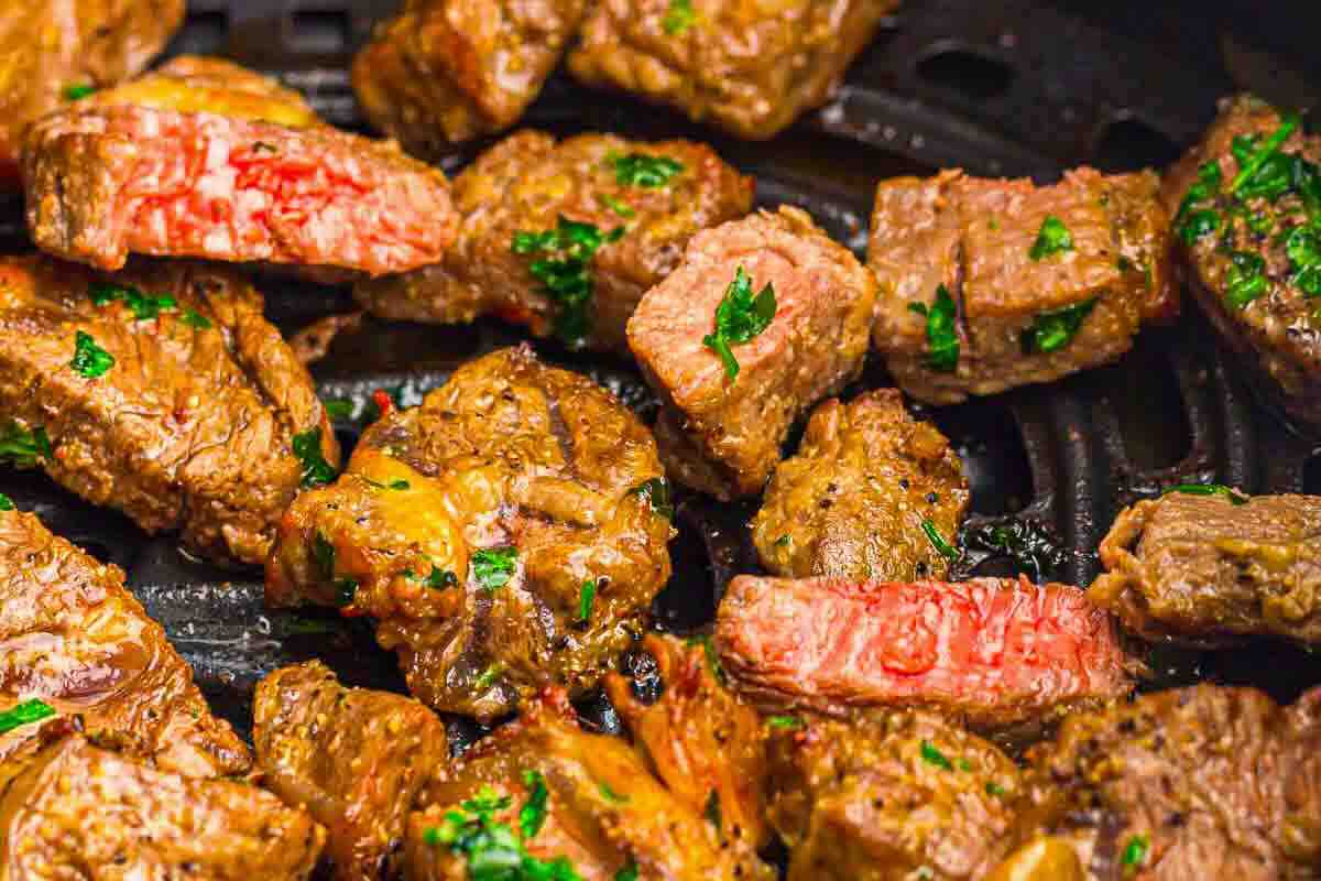 Close-up of cooked steak bites on a black surface, garnished with chopped parsley.