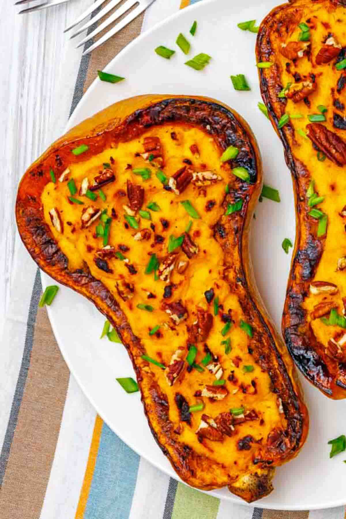 Two roasted butternut squash halves filled with a creamy mixture, topped with chopped pecans and green herbs, served on a white plate.