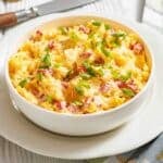 A white bowl filled with scrambled eggs mixed with diced tomatoes and topped with chopped green onions, placed on a white plate.