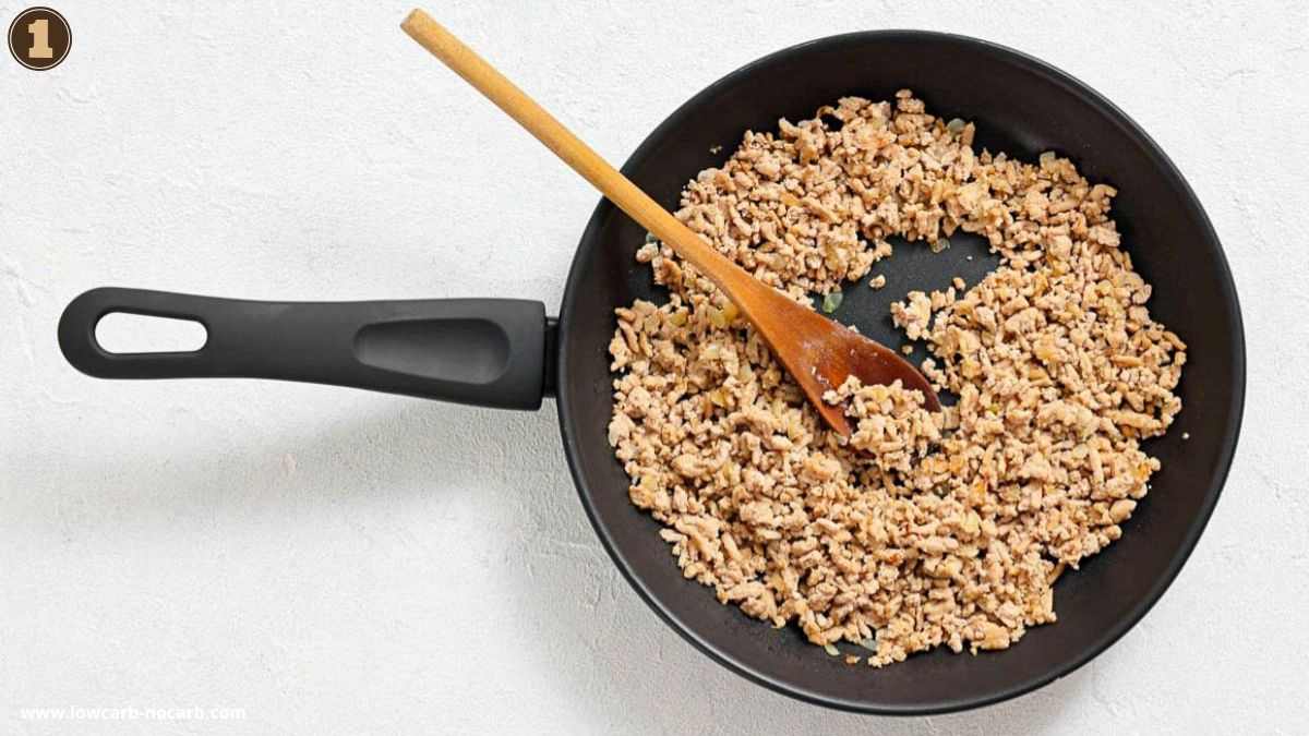 A nonstick frying pan with cooked ground meat and a wooden spoon resting on the side, viewed from above.