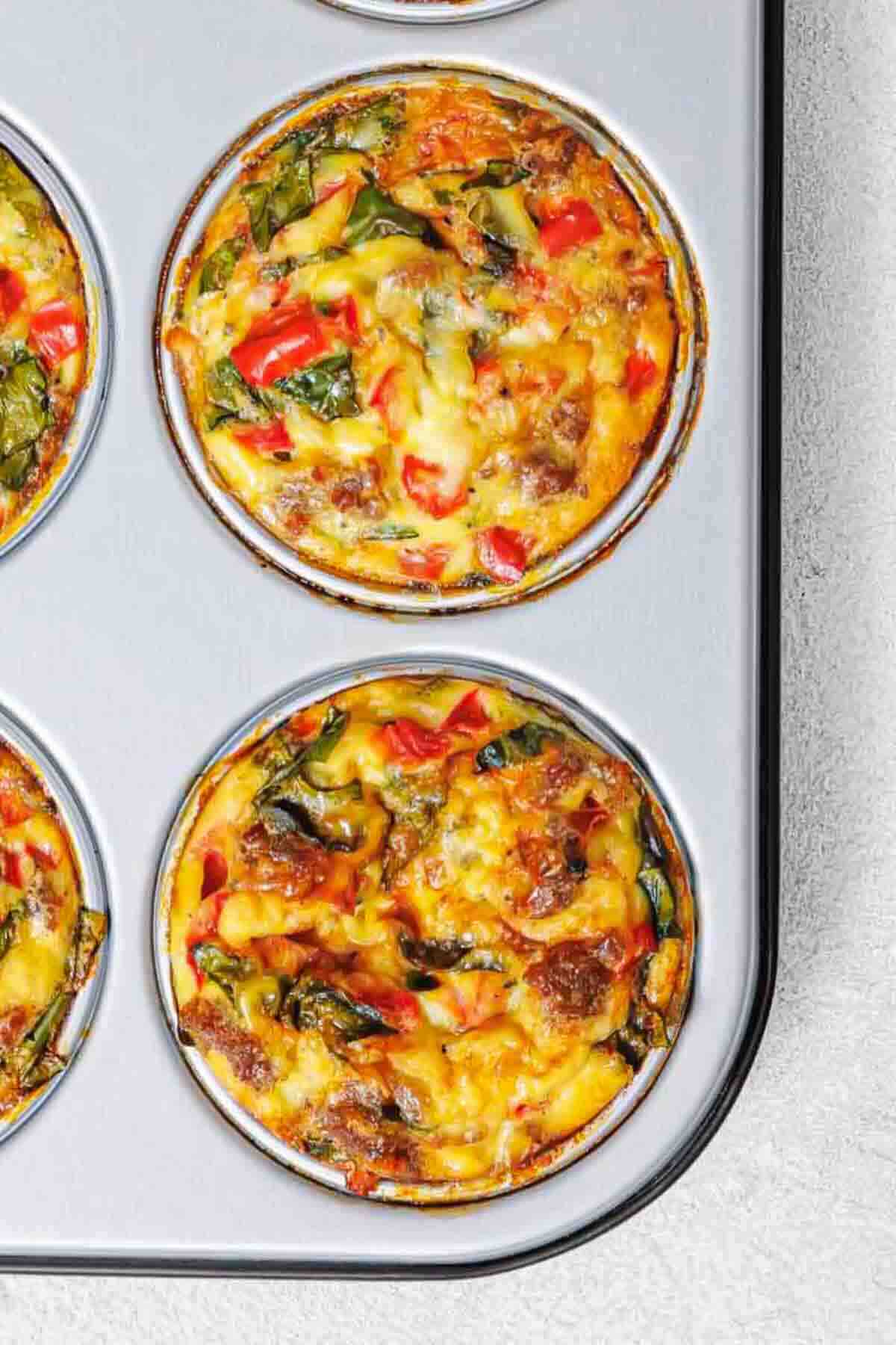 A close-up view of baked egg muffins with vegetables in a metal muffin pan.