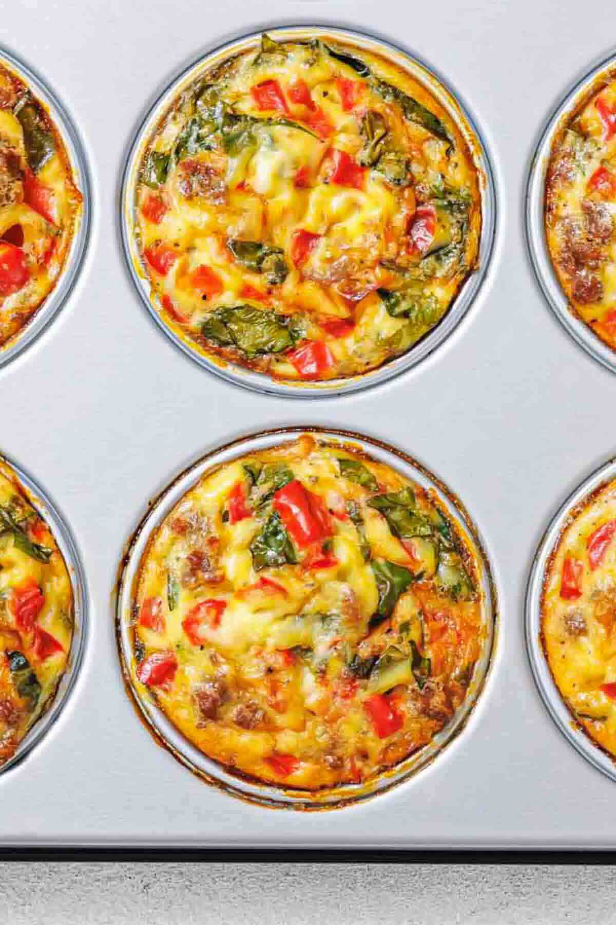 A muffin tin filled with baked egg muffins containing visible pieces of red bell pepper, greens, and cheese.