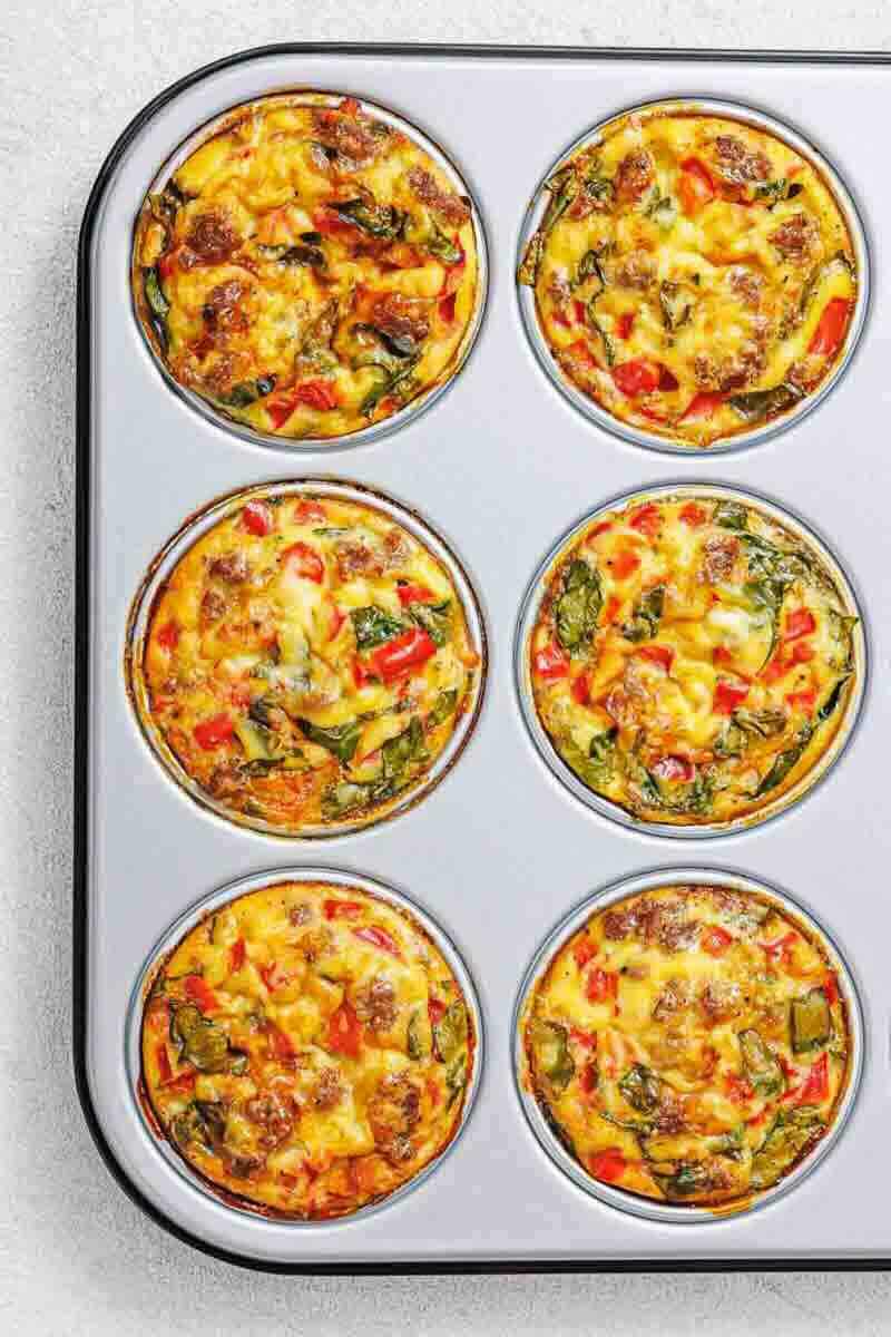 Six baked egg muffins with vegetables and possibly sausage in a muffin tin, viewed from above.
