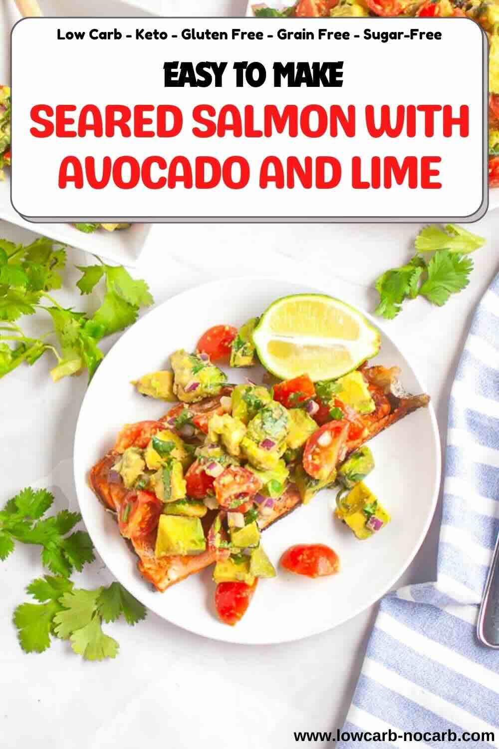 A plate of seared salmon topped with avocado, tomato, and lime relish, garnished with cilantro, with a lime wedge on the side.