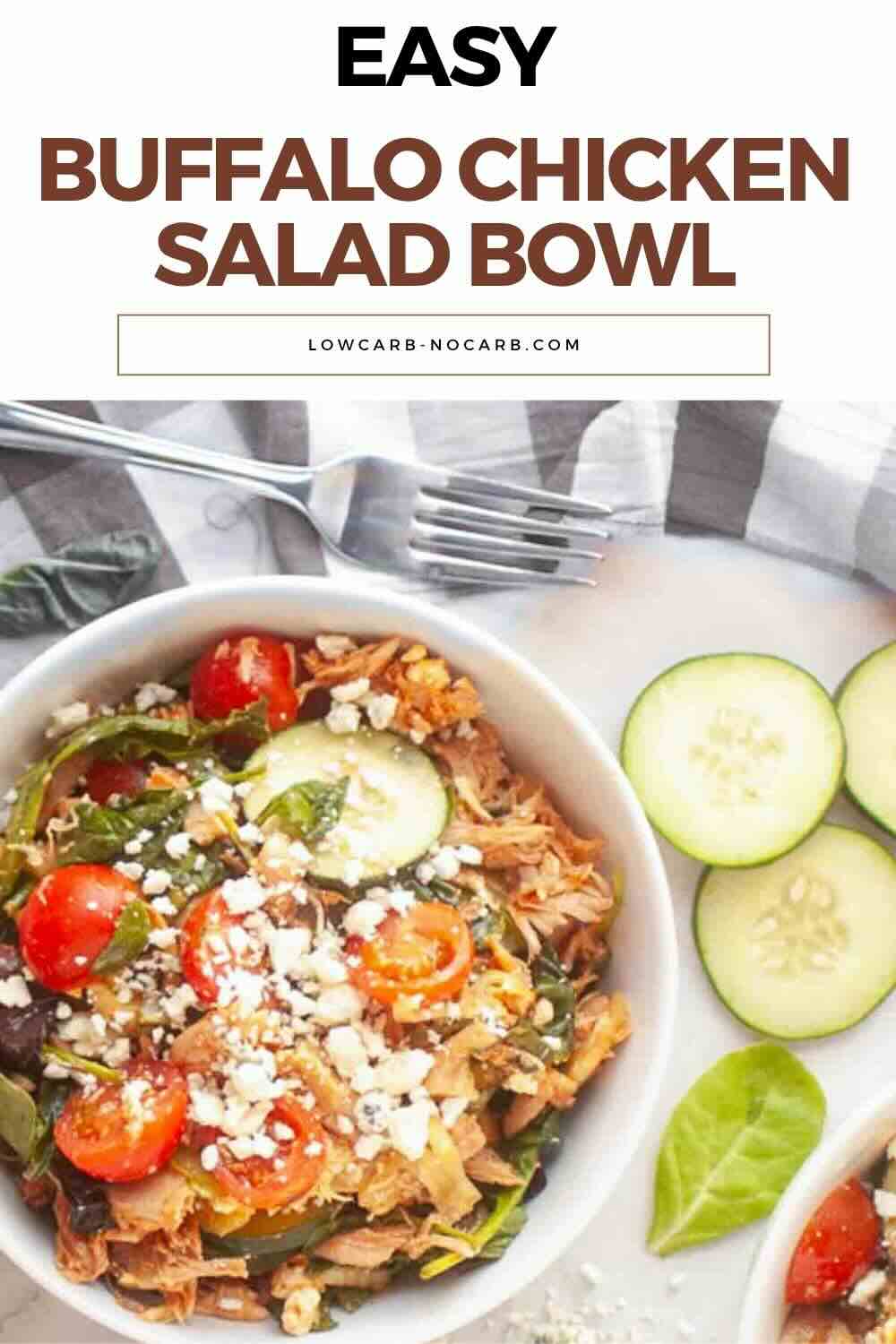 A bowl of buffalo chicken salad with cherry tomatoes, spinach, feta cheese, and sliced cucumbers on the side, set on a white surface with a striped napkin.