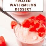 A glass bowl filled with a creamy pink frozen watermelon dessert, topped with watermelon cubes, with a spoon in the bowl and watermelon chunks on the table.