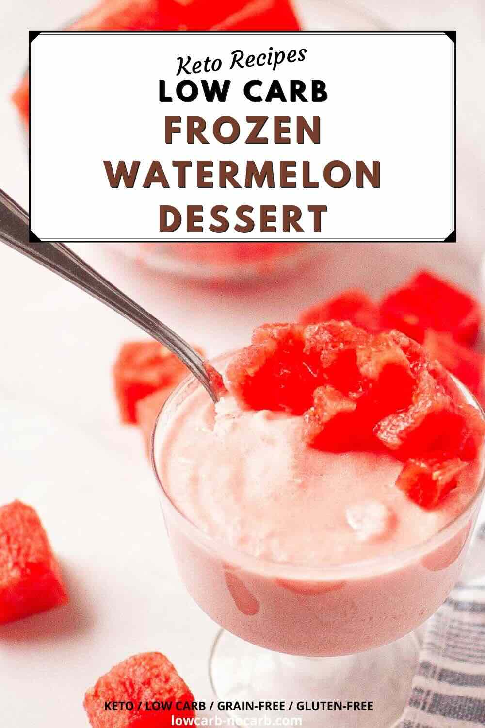 A glass bowl filled with a creamy pink frozen watermelon dessert, topped with watermelon cubes, with a spoon in the bowl and watermelon chunks on the table.
