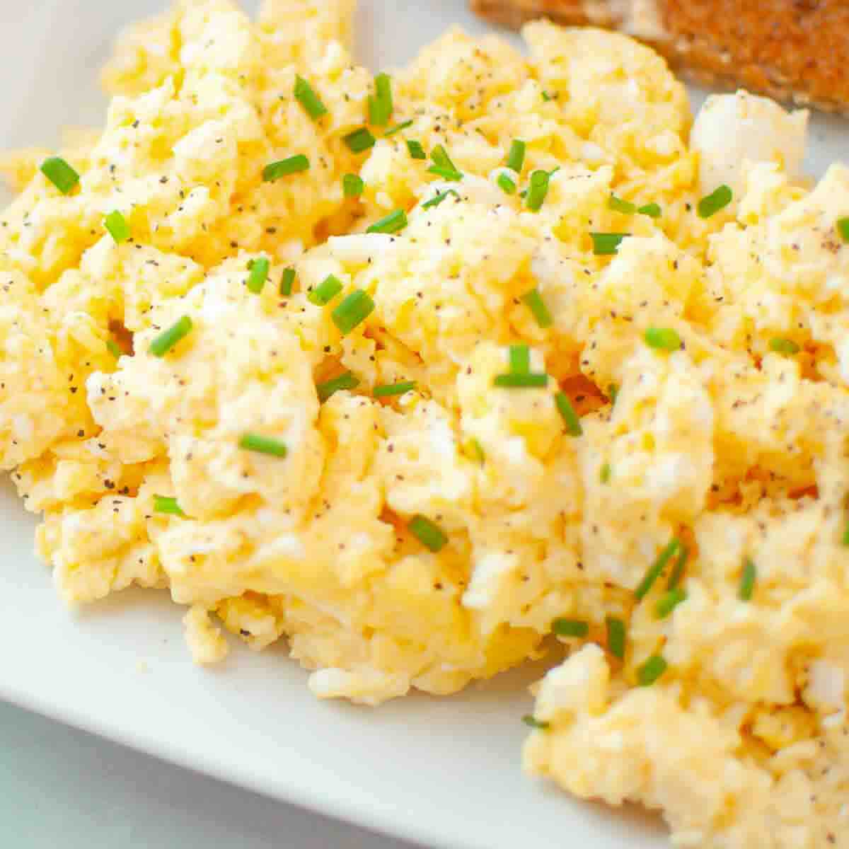 Scrambled eggs garnished with chopped chives and black pepper, served on a white plate.