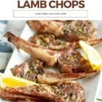 A plate of roasted lamb chops garnished with herbs and served with lemon wedges on a white rectangular dish.