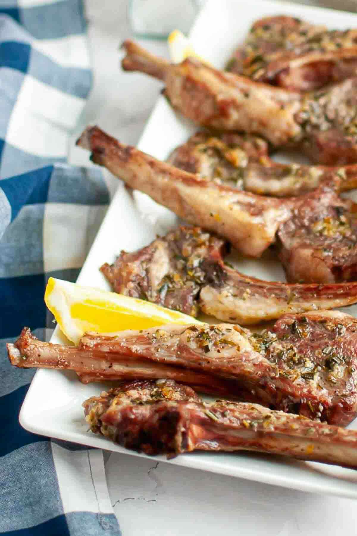 Grilled lamb chops garnished with herbs, served on a white plate with lemon wedges.