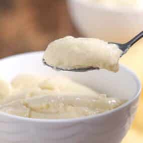 A spoonful of creamy pudding is held above a white bowl filled with more pudding.
