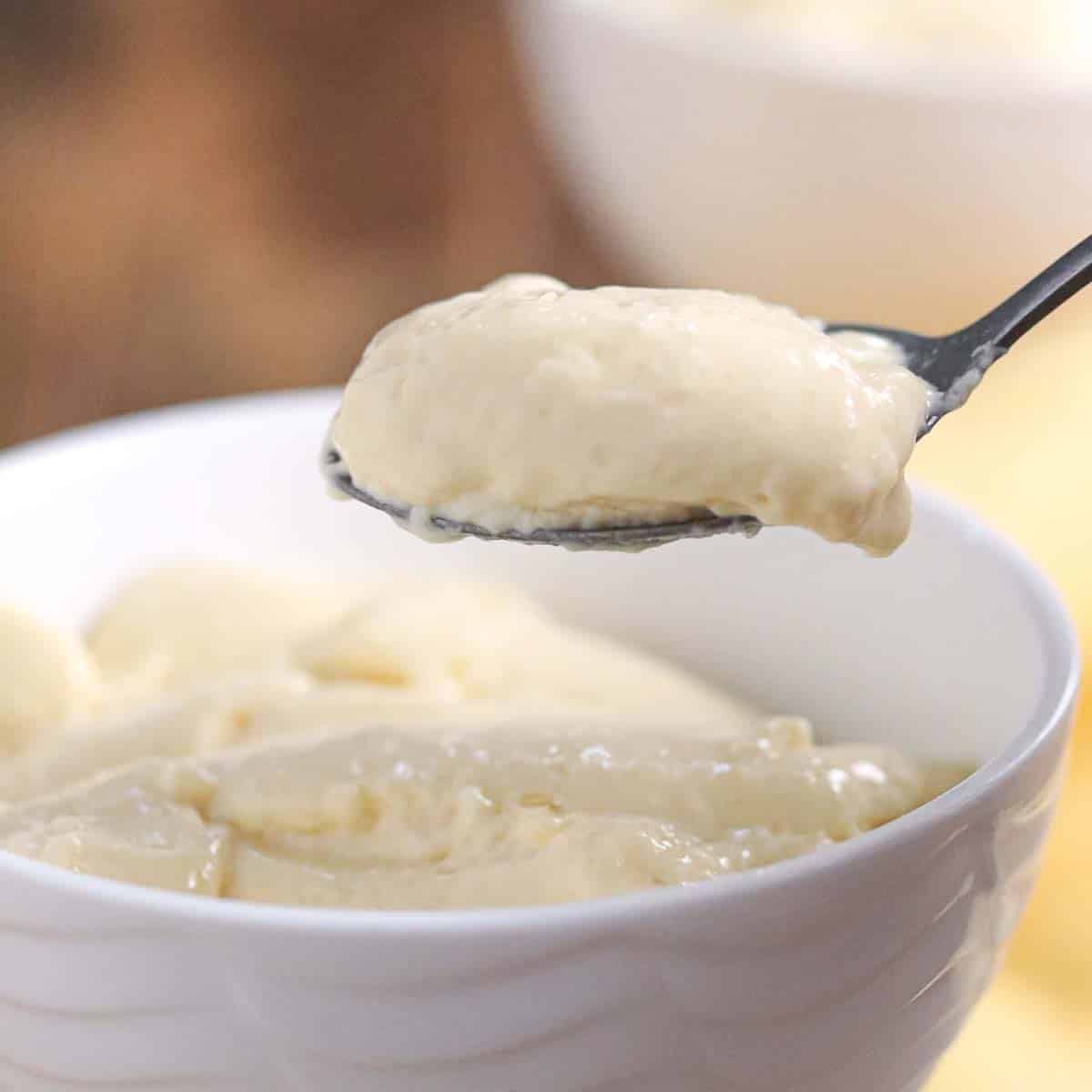 A spoonful of creamy pudding is held above a white bowl filled with more pudding.