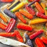 Colorful roasted carrots with herbs on a baking tray, glistening with oil.