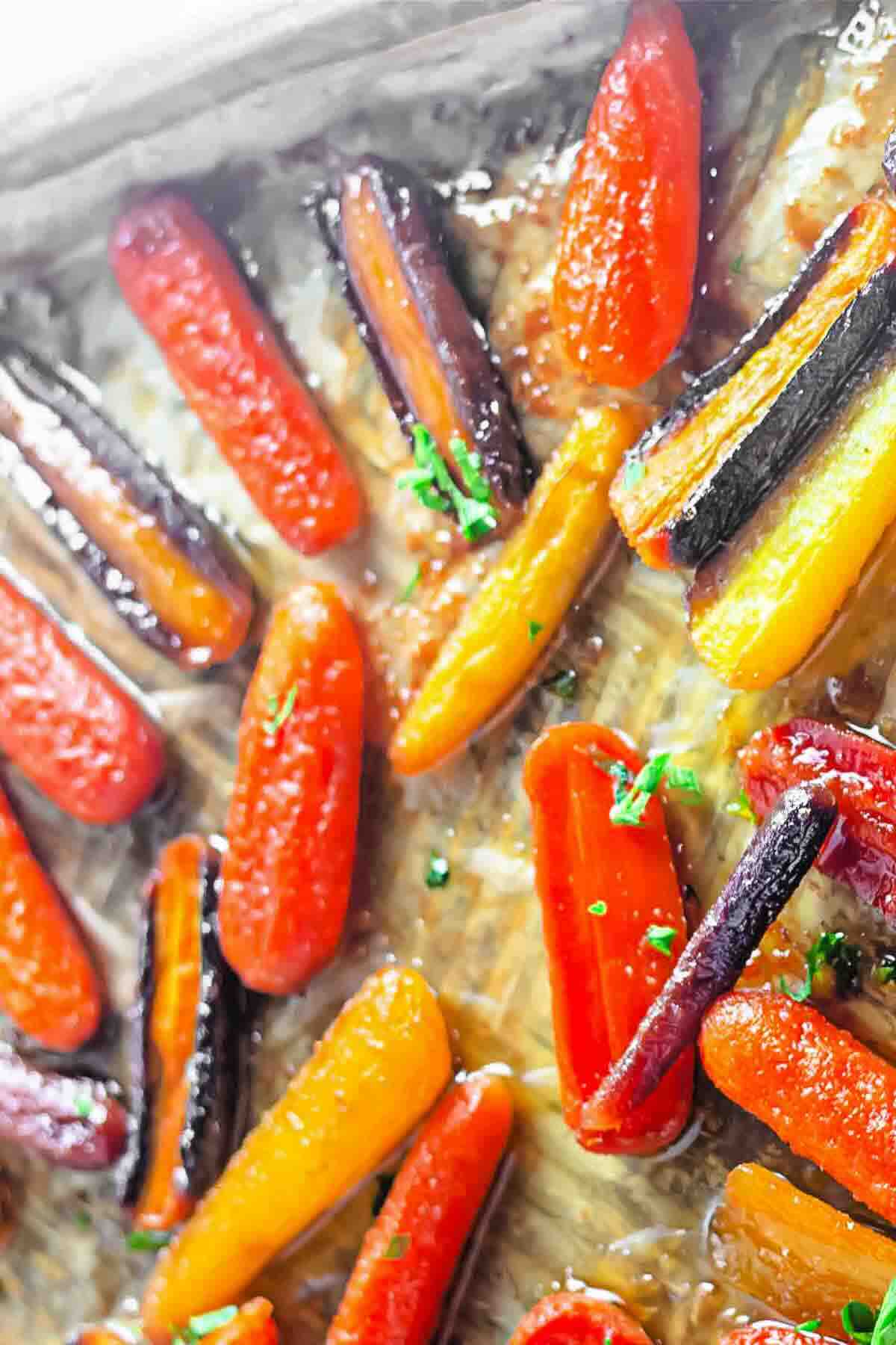 Close-up of roasted multicolored carrots glazed with sauce and garnished with chopped chives on a baking sheet.