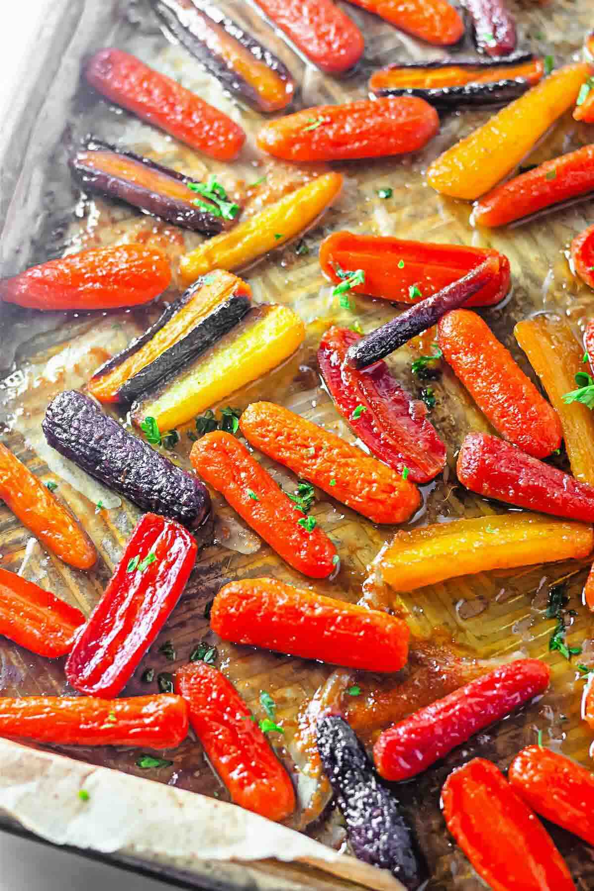 Colorful roasted carrots, including orange, yellow, and purple varieties, arranged on a baking sheet and garnished with chopped herbs.
