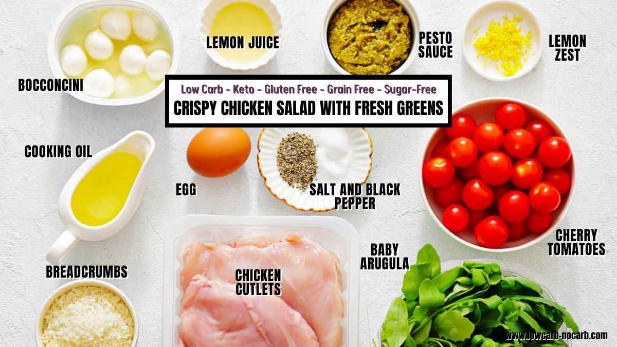 Ingredients for crispy chicken salad with fresh greens are arranged on a white surface, each labeled, including chicken cutlets, egg, breadcrumbs, bocconcini, lemon juice, pesto, and vegetables.