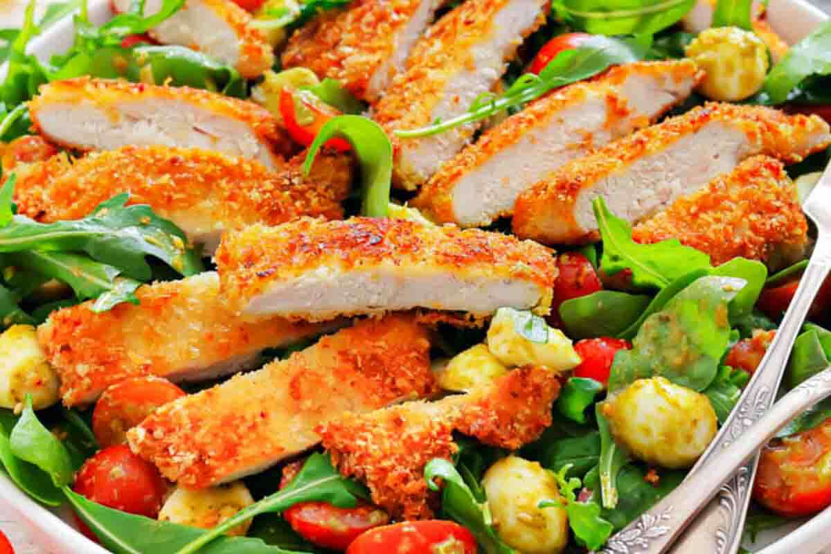 Sliced breaded chicken breast served on a bed of arugula, grape tomatoes, mozzarella balls, and avocado.